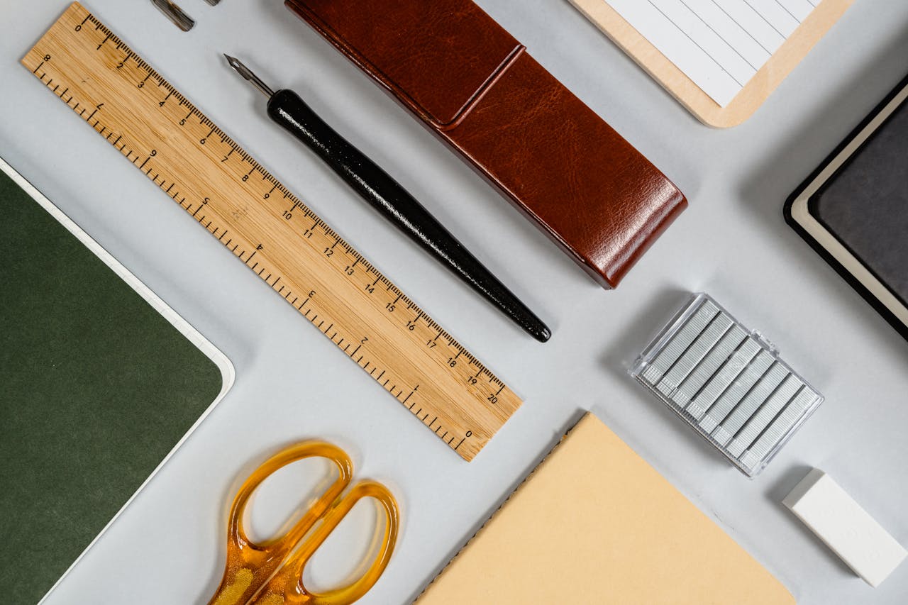A variety of stationery including scissors, ruler, and notebook arranged in an organized flat lay on a desk.
